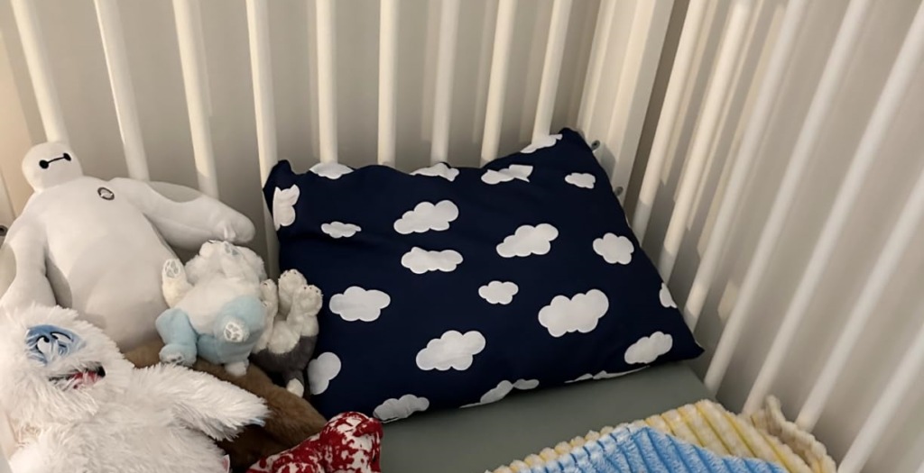 A stuffed animal toy sits on a bed next to a Biloban Toddler Pillow, showcasing its cozy and inviting look.